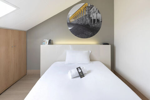 Single bed with white linens and towel in a clean room at B&B Hotel Udine with light wood wardrobe and wall art above bed