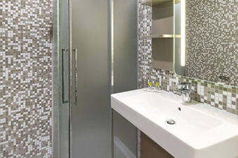 Bathroom sink with faucet, mirror, toiletries, and shower with frosted glass doors in B&B Hotel Udine