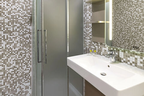 Bathroom sink with faucet, mirror, toiletries, and shower with frosted glass doors in B&B Hotel Udine