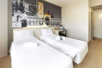 Hotel room at B&B Hotel Udine with two single beds, white linens, desk with laptop, and black and white artwork above beds