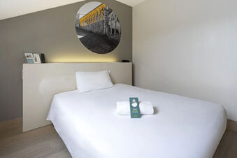 Simple hotel room with a white bed, pillow, towel, and a circular wall photo at B&B Hotel Udine