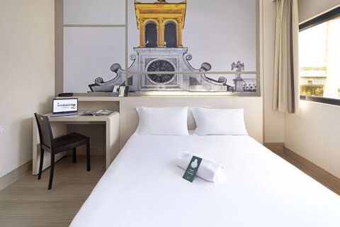 Room at B&B Hotel Udine with white bed and pillows, towel on bed, desk with laptop and window with curtains