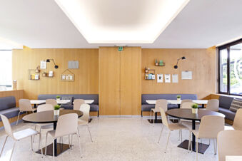Bright dining area at B&B Hotel Udine featuring round and rectangular tables with chairs and bench seating along wooden walls
