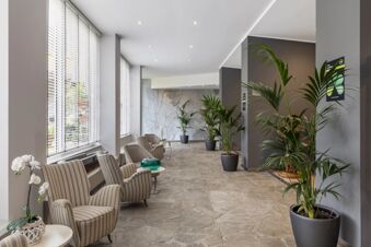 Sitting area with striped armchairs, potted plants, large windows with blinds, and textured stone floor at B&B Hotel Park Hotel Suisse Santa Margherita Ligure