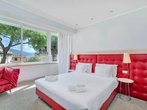 Bright hotel room at B&B Hotel Park Hotel Suisse Santa Margherita Ligure with white bed, red headboard, chair, and large window view