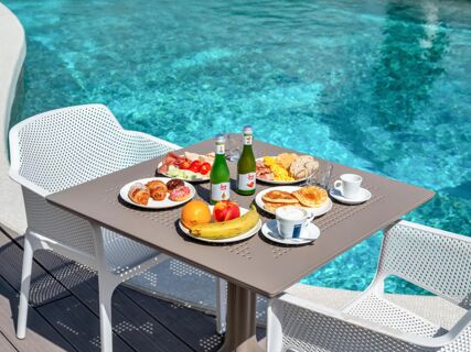Table with breakfast items including croissants, pancakes, fruit, juice bottles, coffee cups by pool at B&B Hotel Park Hotel Suisse Santa Margherita Ligure
