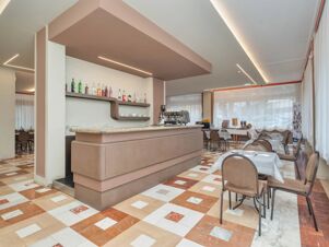 Dining area with tables and chairs, a beige bar counter with liquor bottles, and large windows at B&B Hotel Riviera Celle Ligure
