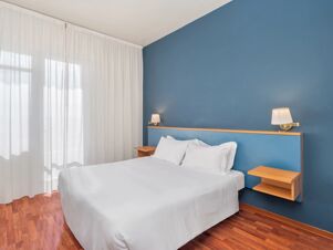 A bed with white linens and pillows against a blue wall with wooden floating nightstands and lamps in B&B Hotel Riviera Celle Ligure