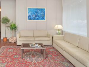 Living room interior of B&B Hotel Riviera Celle Ligure with beige leather sofas, a blue wave painting, plants, and a red patterned rug