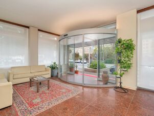 Beige sofas, a patterned red rug, glass revolving door, and several potted plants visible in B&B Hotel Riviera Celle Ligure lobby