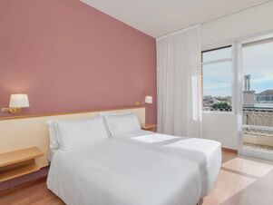 Twin beds with white linens under a dusty pink wall with two brass wall lamps and a window with curtains in B&B Hotel Riviera Celle Ligure