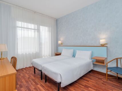 Two single beds with white linens and pillows beside light blue headboards, a desk with lamp, and chair at B&B Hotel Riviera Celle Ligure