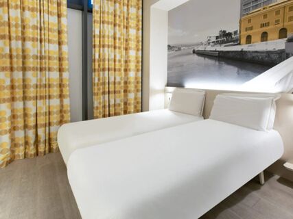 Two single beds with white linens and pillows in a room with yellow and white patterned curtains at B&B Hotel Savona