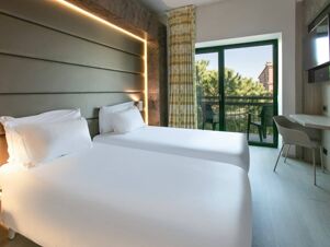 Two single beds with white linens under a padded headboard and balcony with chairs in B&B Hotel Savona room