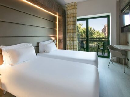 Two single beds with white linens under a padded headboard and balcony with chairs in B&B Hotel Savona room