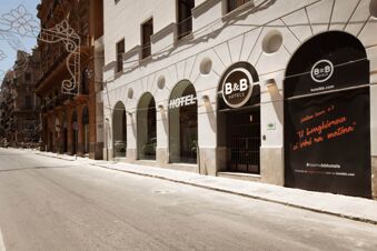 The white exterior of B&B Hotel Palermo Quattro Canti with arched windows, black signs, and adjacent historic buildings on a sunny street