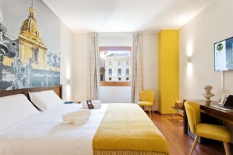 Bright hotel room at B&B Hotel Palermo Quattro Canti with a large bed, yellow accents, wall art, window, and TV on the wall