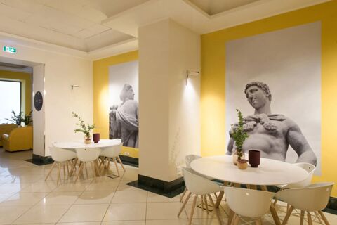 Indoor seating area with white tables and chairs, yellow walls, and black-and-white classical statue images at B&B Hotel Palermo Quattro Canti