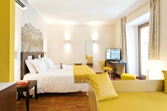 Bright hotel room at B&B Hotel Palermo Quattro Canti featuring a bed with yellow blanket, desk with TV, and yellow sofa with pillows