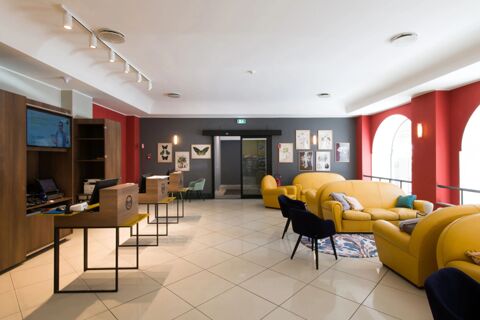 Reception area of B&B Hotel Palermo Quattro Canti with wooden desks, yellow sofas, navy chairs, and botanical wall art