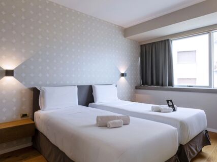 Two neatly made single beds with white linens, rolled towels, and a bedside table in a room at B&B Hotel Trapani Crystal