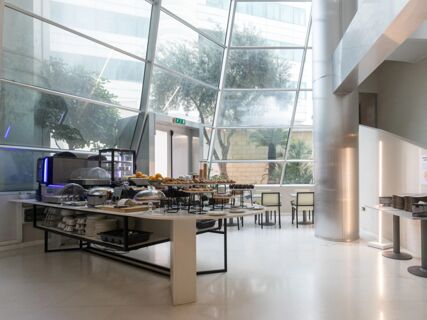 Buffet table with assorted pastries, bread, fruit, and breakfast appliances inside a bright room with large windows at B&B Hotel Trapani Crystal