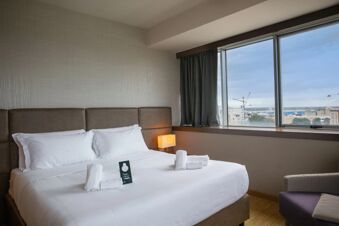 Double bed with white linens and pillows, towels folded on bed, bedside lamp, and window with view at B&B Hotel Trapani Crystal