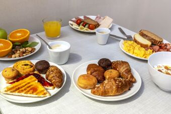 Several plates with croissants, muffins, toast with jam, scrambled eggs, sliced meats, fruits, nuts, coffee, and orange juice at B&B Hotel Trapani Crystal