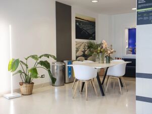 Dining area with white chairs and table, vases with flowers, large potted plant, trash bins, and wall art at B&B Hotel Trapani Crystal
