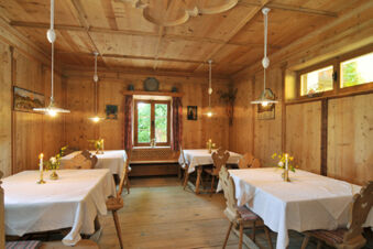 Wood-paneled dining room at Hotel Ansitz Tschindlhof with wooden chairs, tables covered with white linens, candles, and flowers
