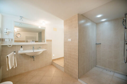 Bathroom with beige tiles, a towel rack, wall-mounted sink, and walk-in shower at Hotel Ansitz Tschindlhof