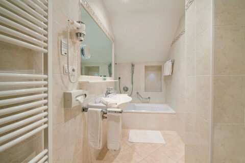 Bathroom at Hotel Ansitz Tschindlhof with beige tiled walls, white bathtub, sink, towels, hairdryer, and wall mirror