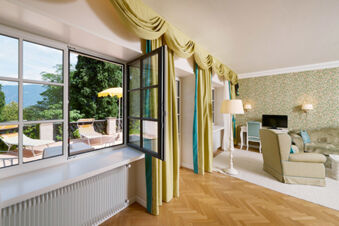 Hotel Ansitz Tschindlhof lounge area with open window, green curtains, parquet floor, floral wallpaper, and outdoor patio visible