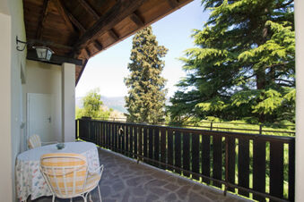 Balcony with table and two chairs overlooking trees and mountains at Hotel Ansitz Tschindlhof in sunlight