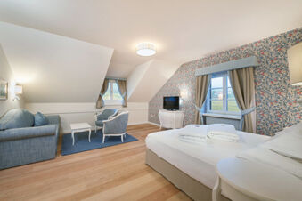 Hotel Ansitz Tschindlhof room with a double bed, folded towels, blue sofa, two armchairs, white table, and floral wallpaper walls