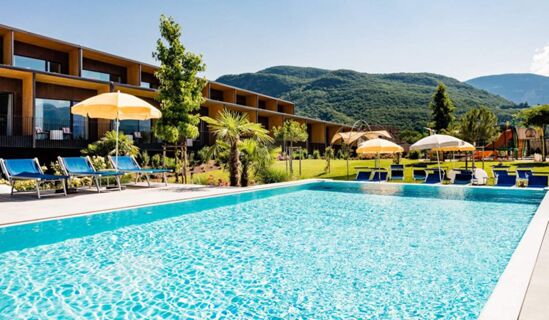 Outdoor swimming pool with blue loungers and yellow umbrellas beside a modern building at Hotel THALHOF am See with green hills in background