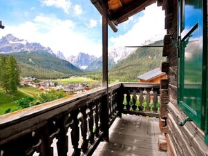 Balkon mit traditionellem Holzgel&auml;nder im Bauernhof Villgrater am Ort mit Blick auf das gr&uuml;ne Tal und die umliegenden Berge bei klarem Himmel.