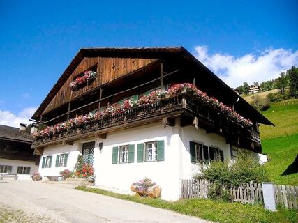 Traditionelles Bauernhaus mit blumengeschm&uuml;ckten Balkonen und gr&uuml;nen Fensterl&auml;den bei Bauernhof Villgrater am Ort unter blauem Himmel in l&auml;ndlicher Umgebung.