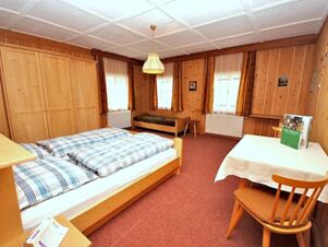 Gem&uuml;tliches Schlafzimmer mit Holzvert&auml;felung, Doppelbett, Einzelbett und Tisch im Bauernhof Villgrater am Ort f&uuml;r erholsame N&auml;chte.