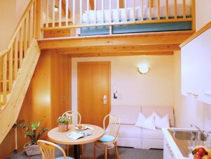 Уютен дневен кът с трапезария, диван и двуетажно легло в стая в Apparthotel Central с обзавеждане от светло дърво.
