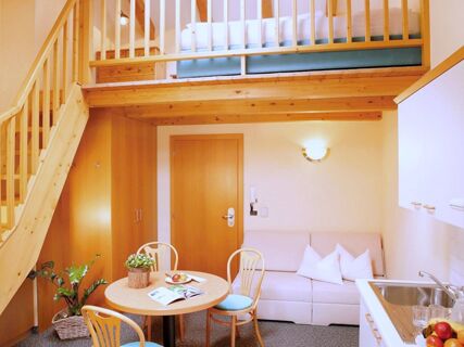 Уютен дневен кът с трапезария, диван и двуетажно легло в стая в Apparthotel Central с обзавеждане от светло дърво.