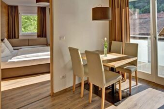 Светло обзаведена трапезария с маса и четири стола и прилежаща спалня в Apparthotel Central с изглед към балкона.