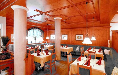 Уютен ресторант с дървени стени и топъл дървен декор в Apparthotel Central, маси с червени салфетки и табуретки.