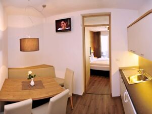 Уютна трапезария с дървена маса, кът за сядане и кухненски бокс в Apparthotel Central, изглед към спалнята с балкон.