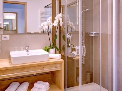 Модерна баня с душ, умивалник, кърпи и орхидея, стилно обзаведена в Apparthotel Central.