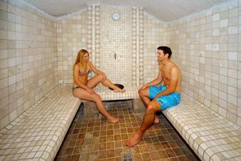 To personer sitter avslappet og vennlig i et flislagt dampbad p&aring; Hotel Waldheim med hvite og brunfargede fliser.