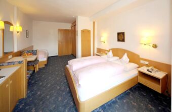 Hotel Waldheim room with a double bed and single bed, wooden furniture, blue patterned carpet, and wall lamps on white walls