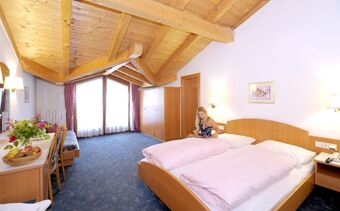 Lyst innredet hotellrom med tretak og store vinduer p&aring; Hotel Waldheim, en kvinne sitter p&aring; sengen i rommet.