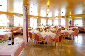 Hotel Waldheim dining area with tables covered in pink and white tablecloths, set with glasses and napkins