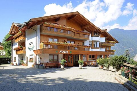 Hotel Waldheim building with wooden balconies adorned with flowers and tables outside under a bright sky with mountains